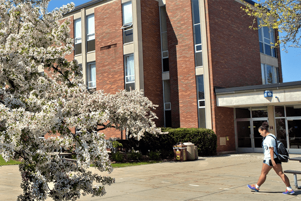 Student walking in front of Dow Science Complex in the spring.