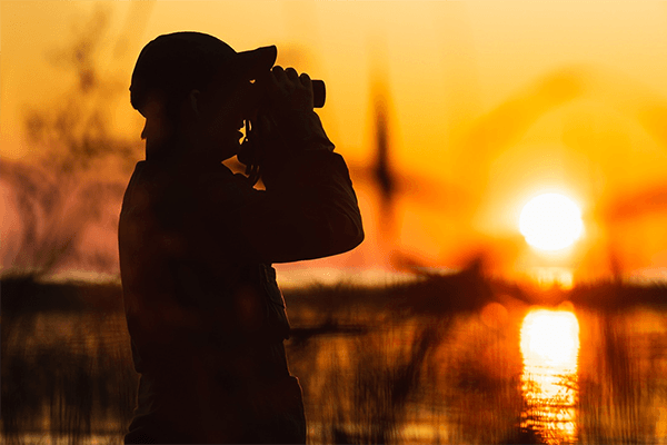 Environmental student looking through binoculars with sun setting behind them