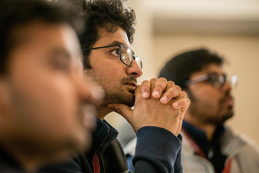A student wearing glasses with his hands on his chin in the middle of two other students.