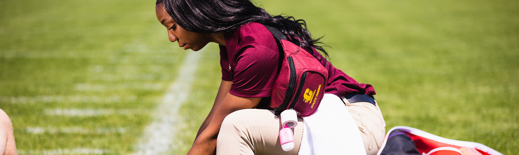 An athletic training student kneeling on a grass field.