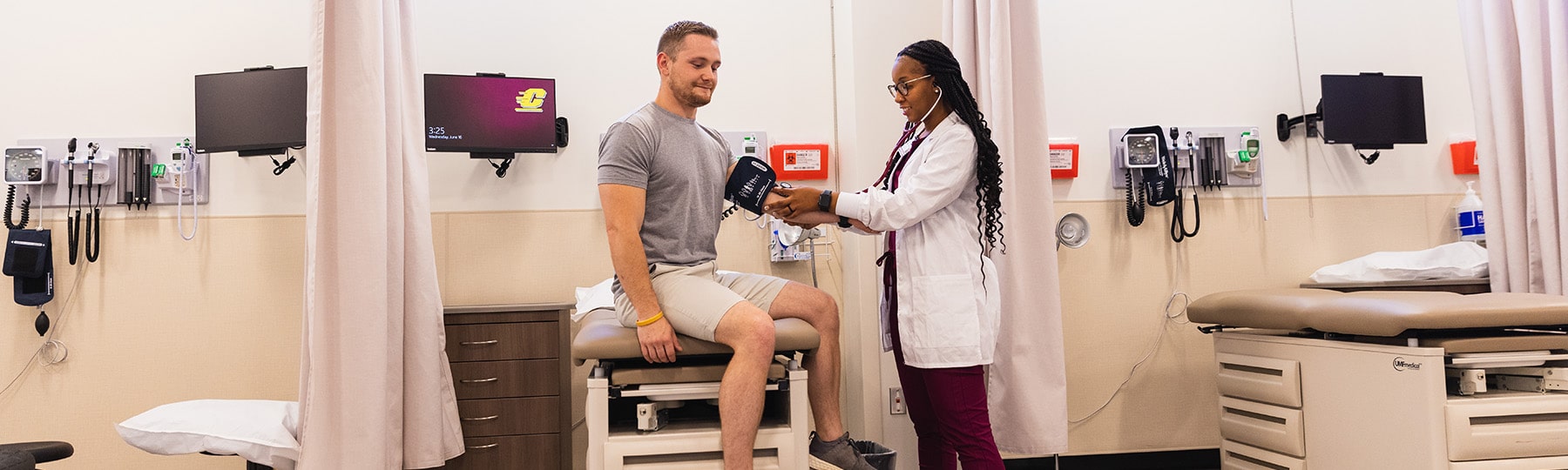 A Central Michigan University physician assistant student stands next to another student to practice taking their blood pressure using a stethoscope and blood pressure cuff.