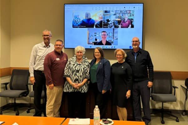 The College of Health Professions Deans Alumni Advisory Board 600x400 Five CMU alumni stand together with the Dean of the College of Health Professions along with two virtual alumni presented on the screen in the background. All are smiling at the camera.