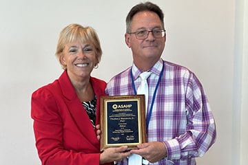 Dean Tom Masterson poses with an Association of Schools Advancing Health Professions representative holding an ASAHP Fellow Award plaque.
