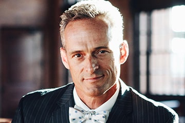 Ron Edwards wearing a suit and bow-tie in a sunlit building.