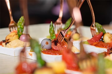 Small boxed appetizers with small rose gold forks inserted in the center of each appetizer on a white platter.