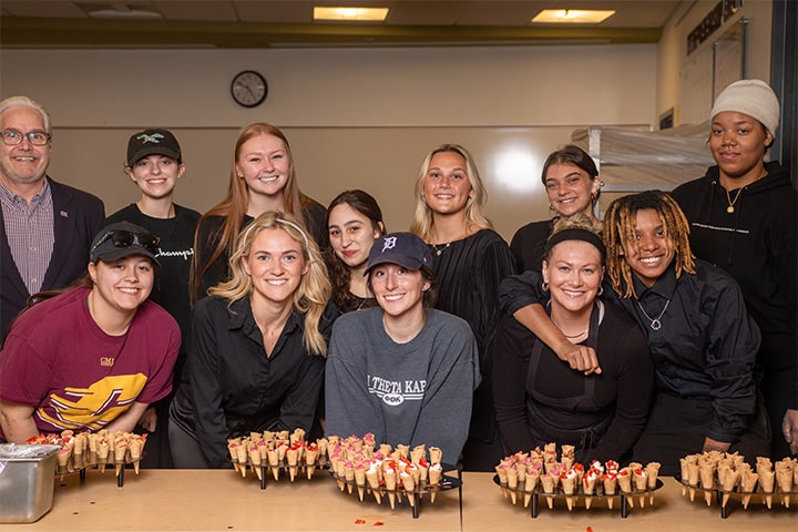 Eleven students pose together with Dr. Fisher in front of a table in the test kitchen on campus.
