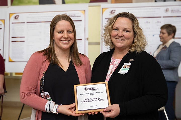 Two people pose holding a College of Health Professions Community Partnership Award plaque.