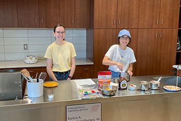 Two students pose together behind a cooking station in the test kitchen on campus.