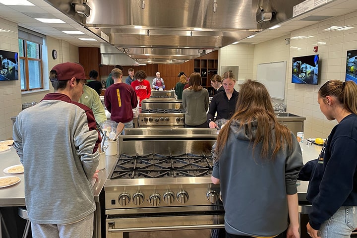 Students participating in a cooking demonstration event in a test kitchen on campus.