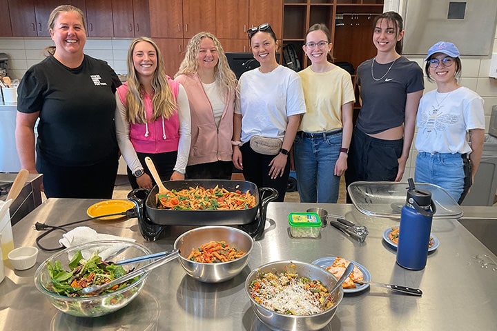 Seven students pose together behind a table of prepared food in the test kitchen on campus.