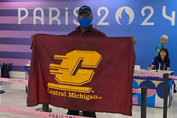 Dr. Vincent Mumford wearing a face mask poses holding a Central Michigan University flag.