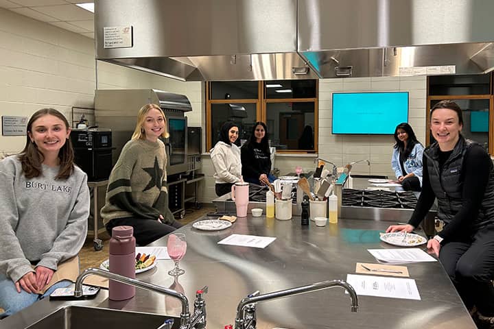 Five students sitting around a stainless-steel cooking station.