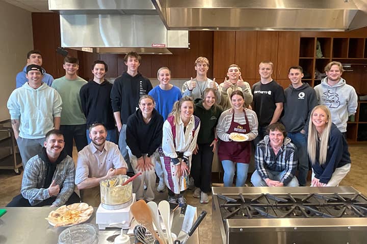 Students pose together in front of a cooking station in the test kitchen on campus.