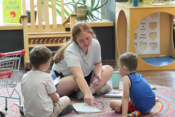 A speech-language pathology student sits on a colorful rug on the floor to work with two children during the Speech Language Pathology Summer Specialty Clinic.