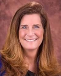 Beth Charlton, wearing a black shirt, stands in front of a brown backdrop and smiles at the camera.