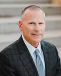 Brian Peters wearing a black jacket, white collared shirt, and light blue tie, stands in front of concrete steps and smiles at the camera.
