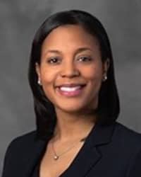 Shanna Johnson, wearing a black shirt and a necklace, stands in front of a dark gray backdrop and smiles at the camera.