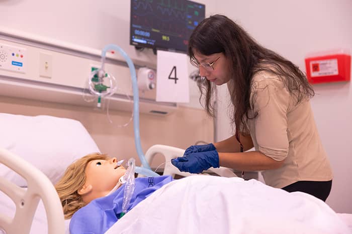 A student works on a simulation mannequin in a hospital bed in the Interprofessional Education and Practice Center.
