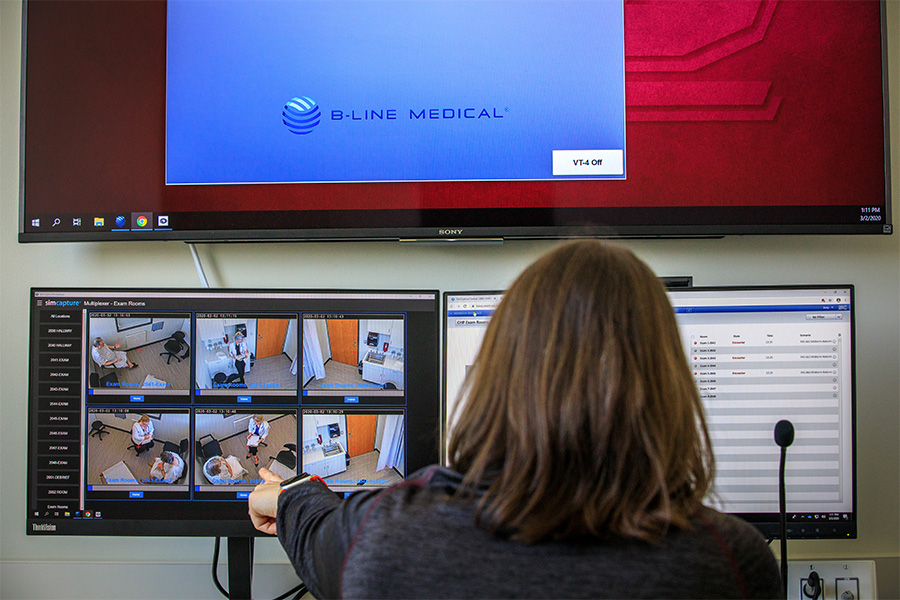 A woman looking at two computer screens and pointing to one of the video camera feeds