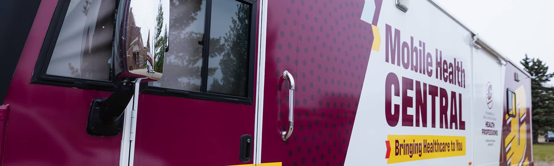 The maroon and white Mobile Health Central bus with Mobile Health Central painted in maroon and Bringing Healthcare to You in maroon on a yellow banner.