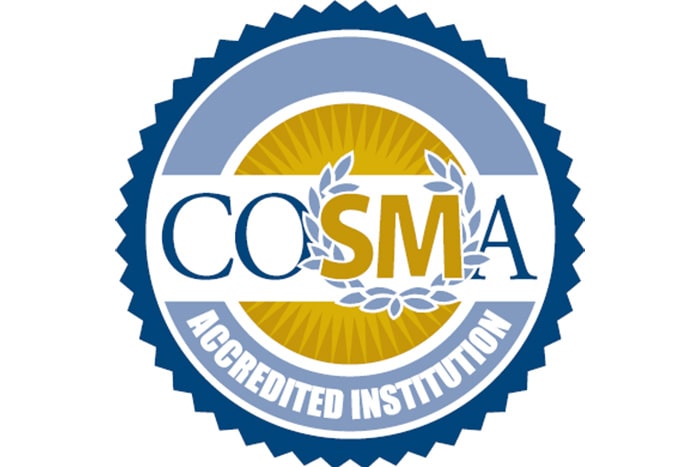 A blue seal with the words accredited institution at the bottom. In the middle of the seal is a gold circle with a white band. The acronym COSMA is centered in the white band in blue and gold with an olive branch symbol surround the SM in COSMA.