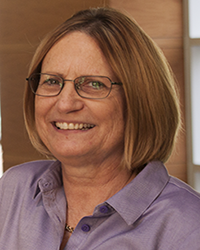 Debbie Silkwood-Sherer wears a light purple shirt and glasses while looking at the camera.