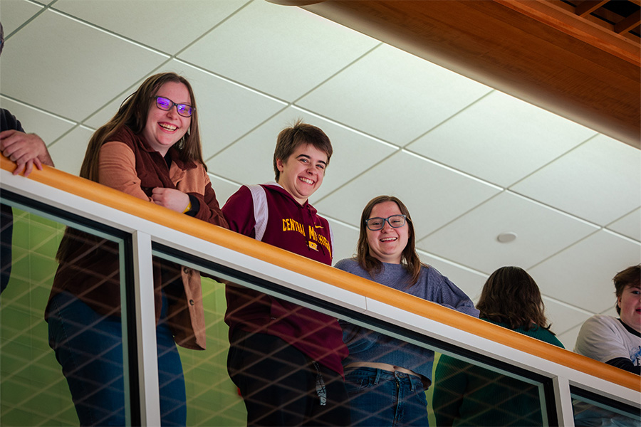 Three students look down from the balcony in The Herbert H. and Grace A. Dow College of Health Professions building.