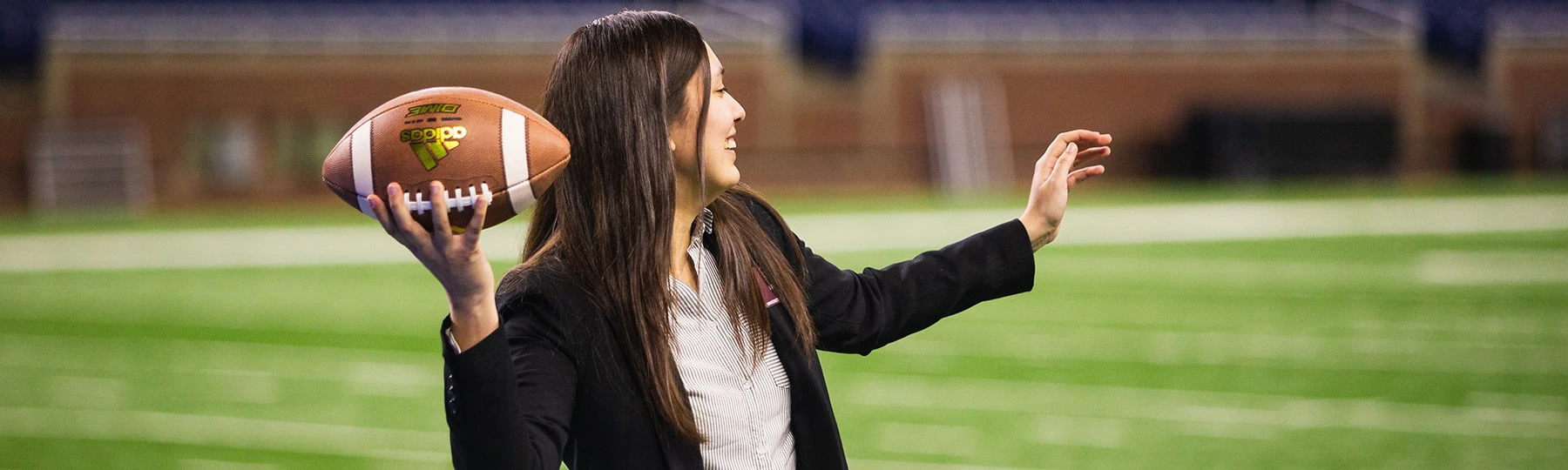 A Central Michigan University sport management student throws a football on the turf of Ford Field