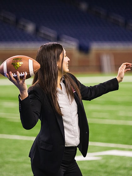 A Central Michigan University sport management student throws a football on the turf of Ford Field