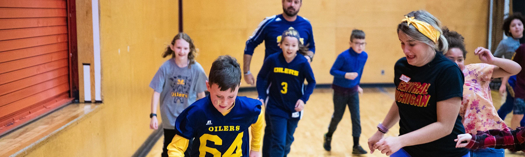 A physical education instructor plays indoor soccer with elementary school students.