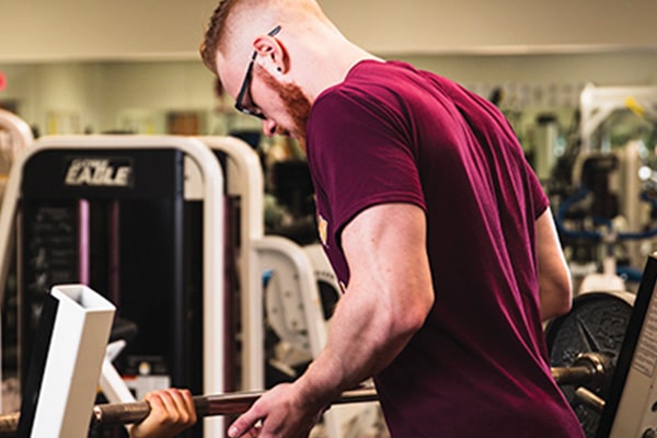 Student assisting an individual lifting weights.