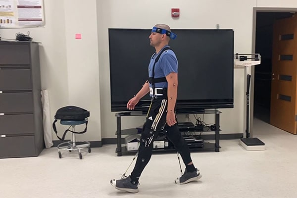 A physical therapy student wearing the NewGait rehabilitative device walks across the Motion Analysis Center lab.