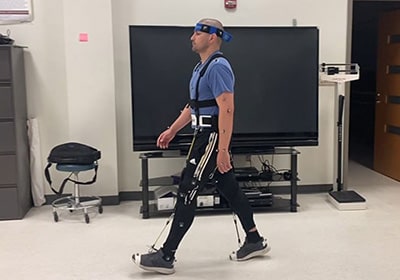 A physical therapy student wearing the NewGait rehabilitative device walks across the Motion Analysis Center lab.