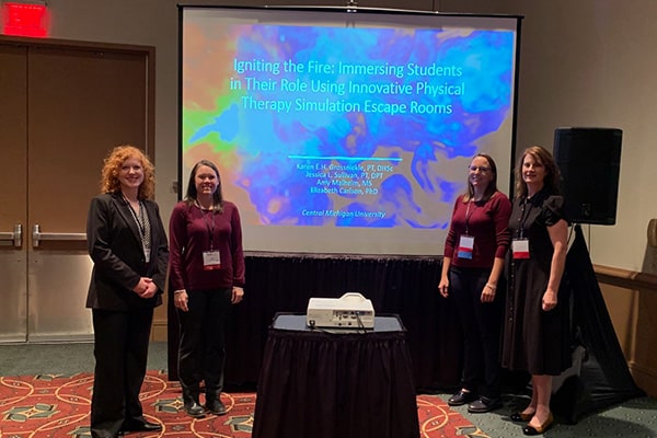 Dr. Karen Grossnickle, Dr. Jessica Sullivan, Dr. Elizabeth Carlson, and Amy Malheim pose in front of their research presentation at a conference.