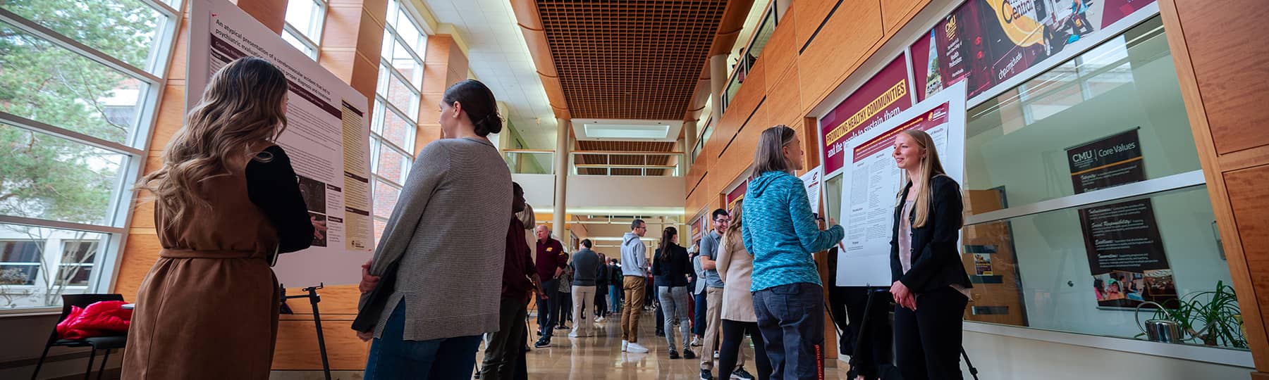 Students, faculty, and staff viewing posters and conversing with presenters at the College of Health Professions Research Symposium.