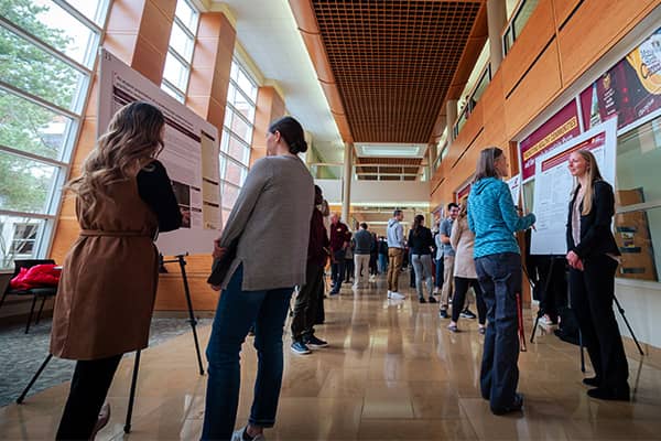 Students, faculty, and staff viewing posters and conversing with presenters at the College of Health Professions Research Symposium.