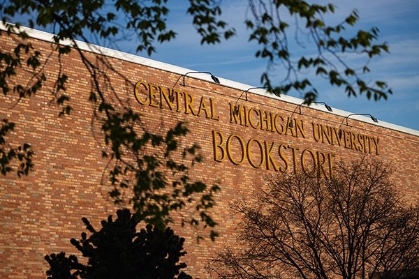 Exterior of CMU Bookstore with brown brick, gold lettering on the side of the building and green tree branches.