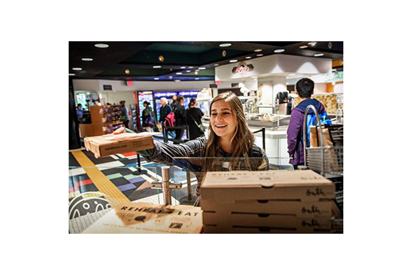 A student holds a pizza box in front of a pizza station in the Central Eats food court at Central Michigan University.