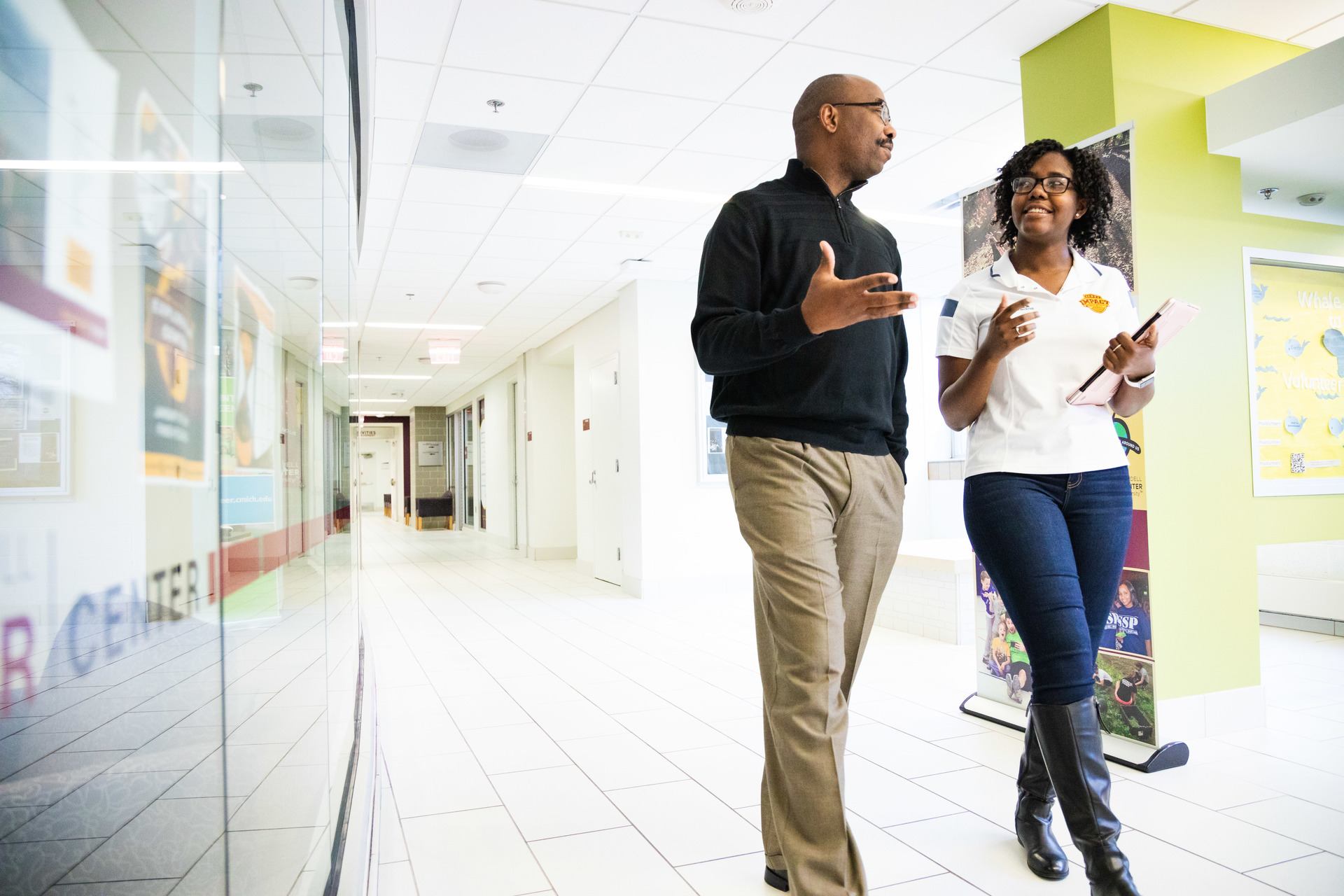 Two people walking through a hallway and talking.