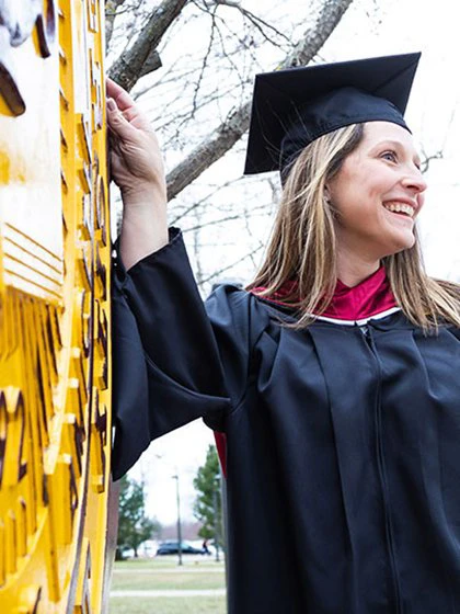 Proud graduate in cap and gown posing for picture by university seal