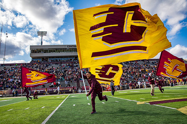CMU Homecoming Students on the Football Field running with CMU Flags.