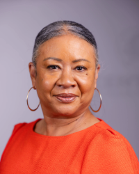 A woman in a bright colored top smiling in front of a light grey background