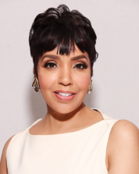 A woman in a light colored top smiling in front of a white background