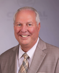 A man in a light colored suit smiling in front of a light grey background.