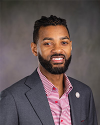 Professional headshot of Trustee Isaiah Oliver with a striped shirt in front of a grey background.