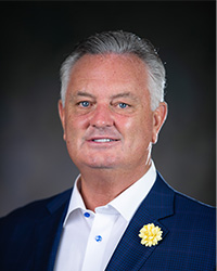 Professional headshot of Trustee Todd J. Anson in a blue suit in front of a grey background.