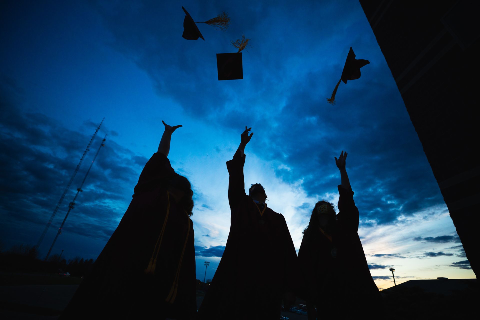 Silhouetted students toss their graduation caps into the air.