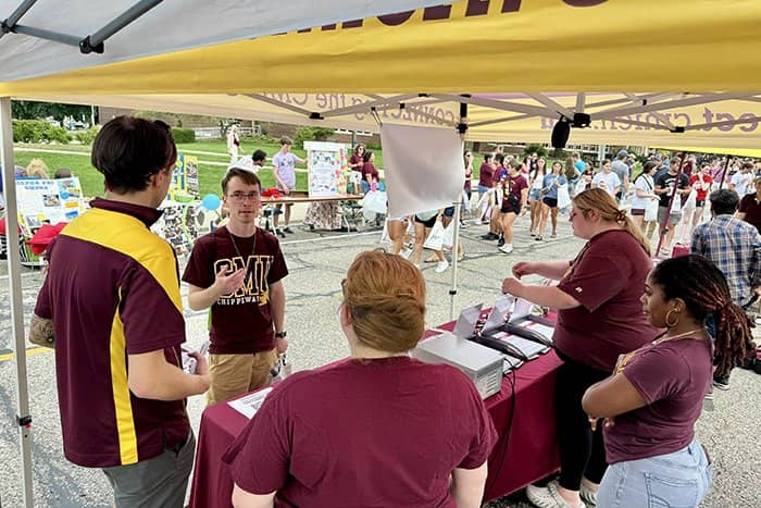 Four OIT staff members converse with a student under a tent.