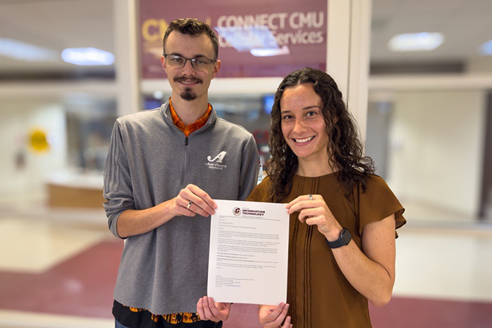 Ashley presents a scholarship award letter to Brian while standing in front of the CONNECT CMU sign.
