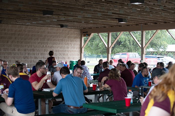 Wide shot of many staff enjoying lunch under a park pavilion.